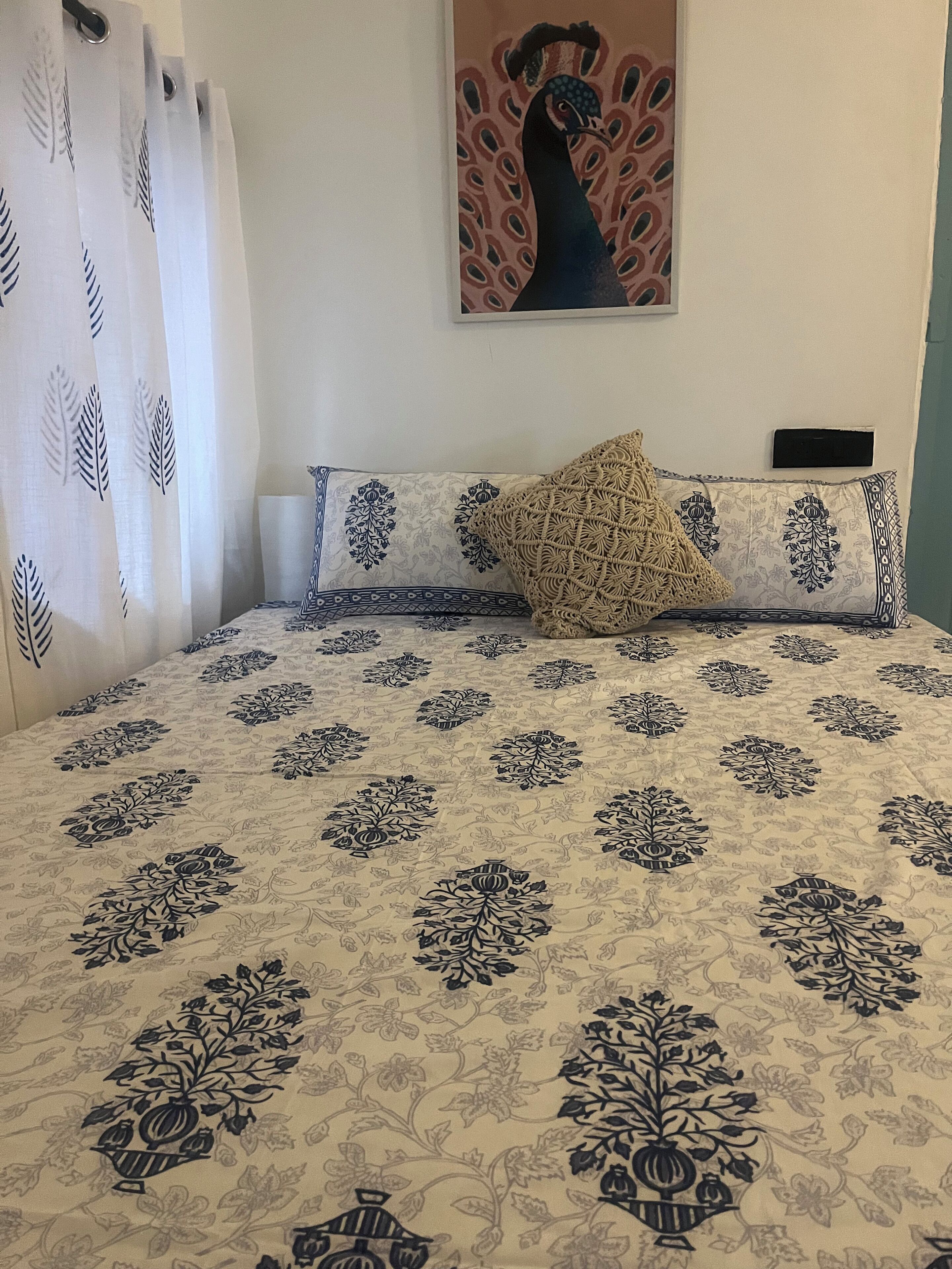 A bed with a patterned bedspread, a decorative pillow, a wall-mounted painting, and a curtain with a leaf pattern.
