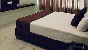 A hotel room with a bed, a TV mounted on the wall, a ceiling fan, and a window with curtains. - Anandam Hotel (Pindra)