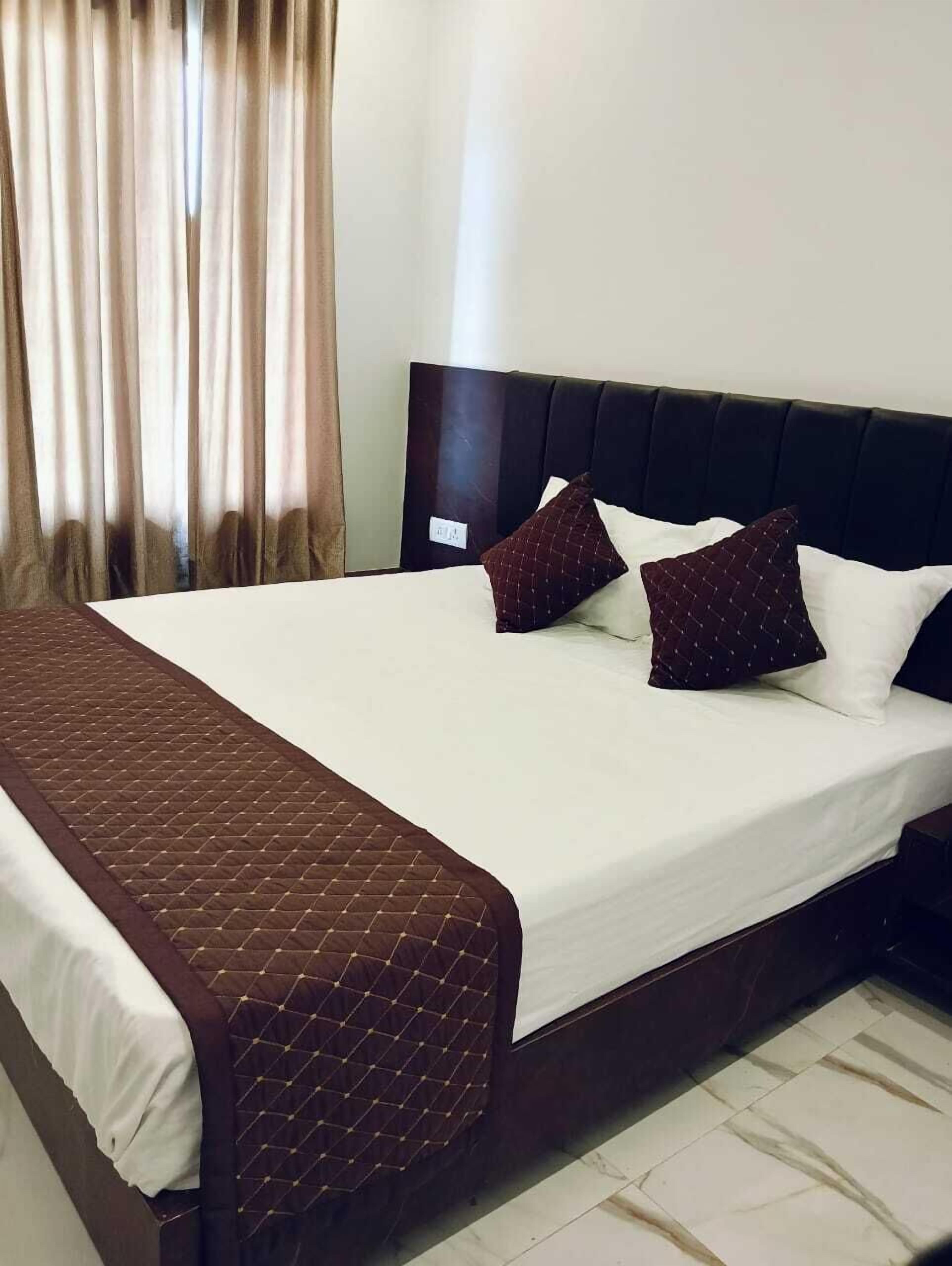 Una cama bien tendida con un cabecero oscuro, ropa de cama blanca y dos almohadas estampadas.