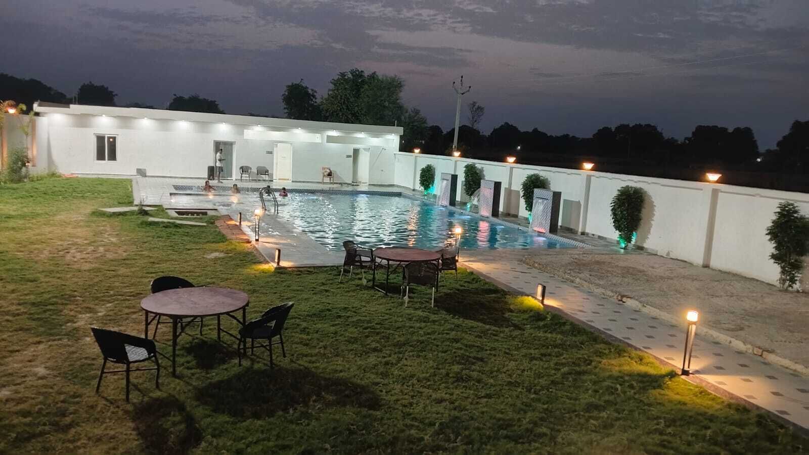 Una piscina con zona de patio, asientos exteriores y un edificio con varias puertas.