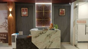 A reception desk with a marble top, two framed pictures on the wall, and a sign that reads "MAGNA". - Anandam Hotel (Pindra)