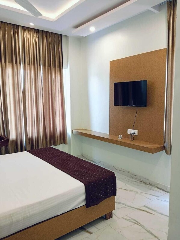Une chambre d’hôtel avec un lit, un téléviseur fixé au mur et une fenêtre avec des rideaux.