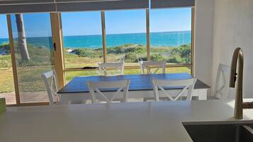 Une cuisine avec vue sur l’océan, une table à manger avec des chaises et un lave-vaisselle Bosch.