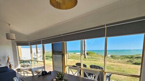 A modern dining area with a large table and chairs, a hanging light fixture, and a view of the ocean. - Oceanfront retreat with breathtaking views steps from the shore. (Ledge Point)