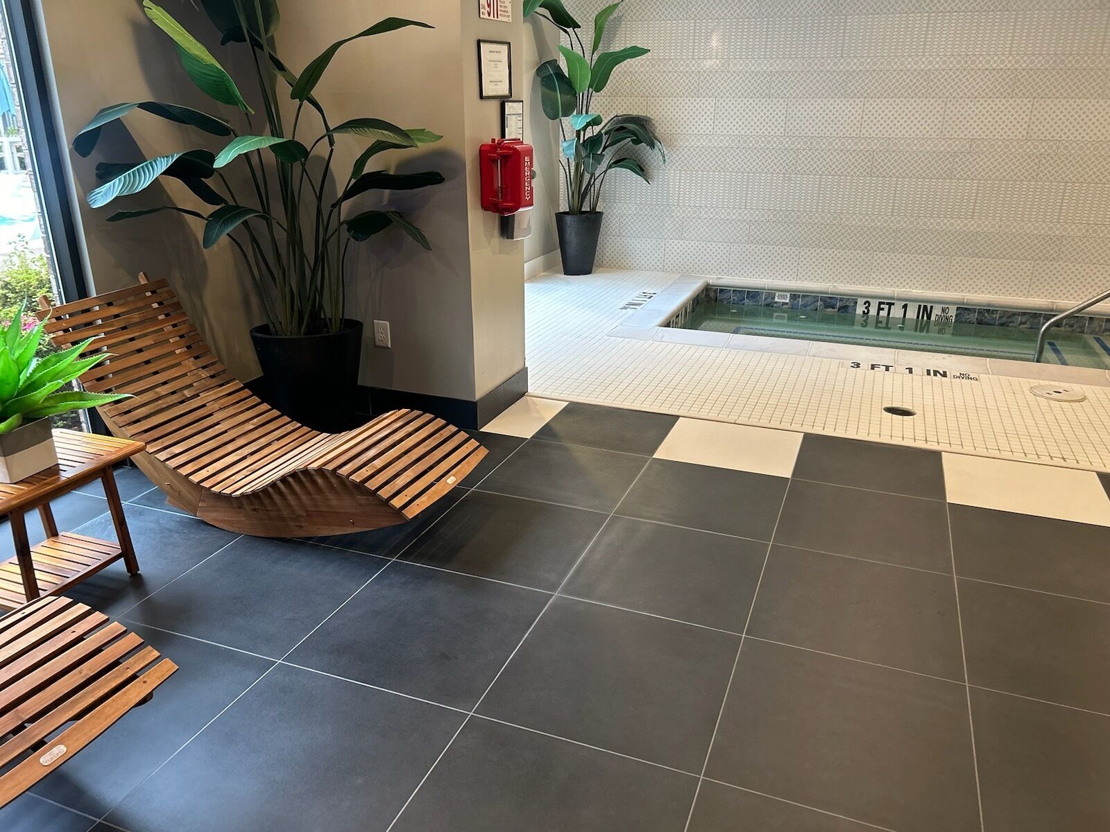 A modern indoor area with a wooden bench, potted plants, and a tiled floor.
