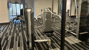 Een sportschool met trainingsapparatuur, een vloer met patroon en een groot raam met uitzicht op bomen.