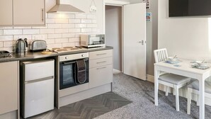 A compact kitchen with a microwave, toaster, kettle, oven, and a dining area with a table and chairs. - A great apartment so close to the beach and harbour and within the town centre. (Bridlington)