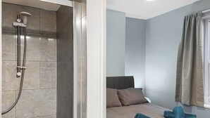 Un bagno con doccia, un letto con cuscini e una finestra con tende.