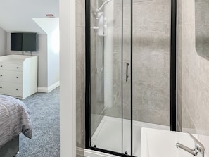 A modern bathroom with a glass-enclosed shower, a white sink, and a flat-screen TV mounted on the wall.