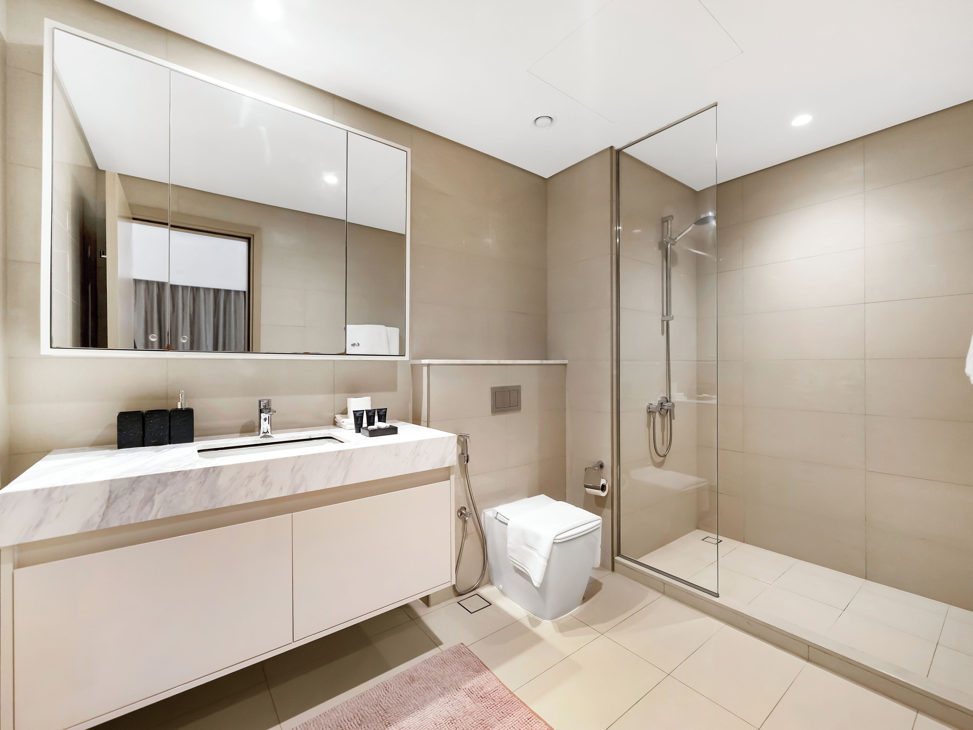 Et moderne badeværelse med et stort spejl, en marmorvask, en glasafskærmet brusekabine og et toilet.