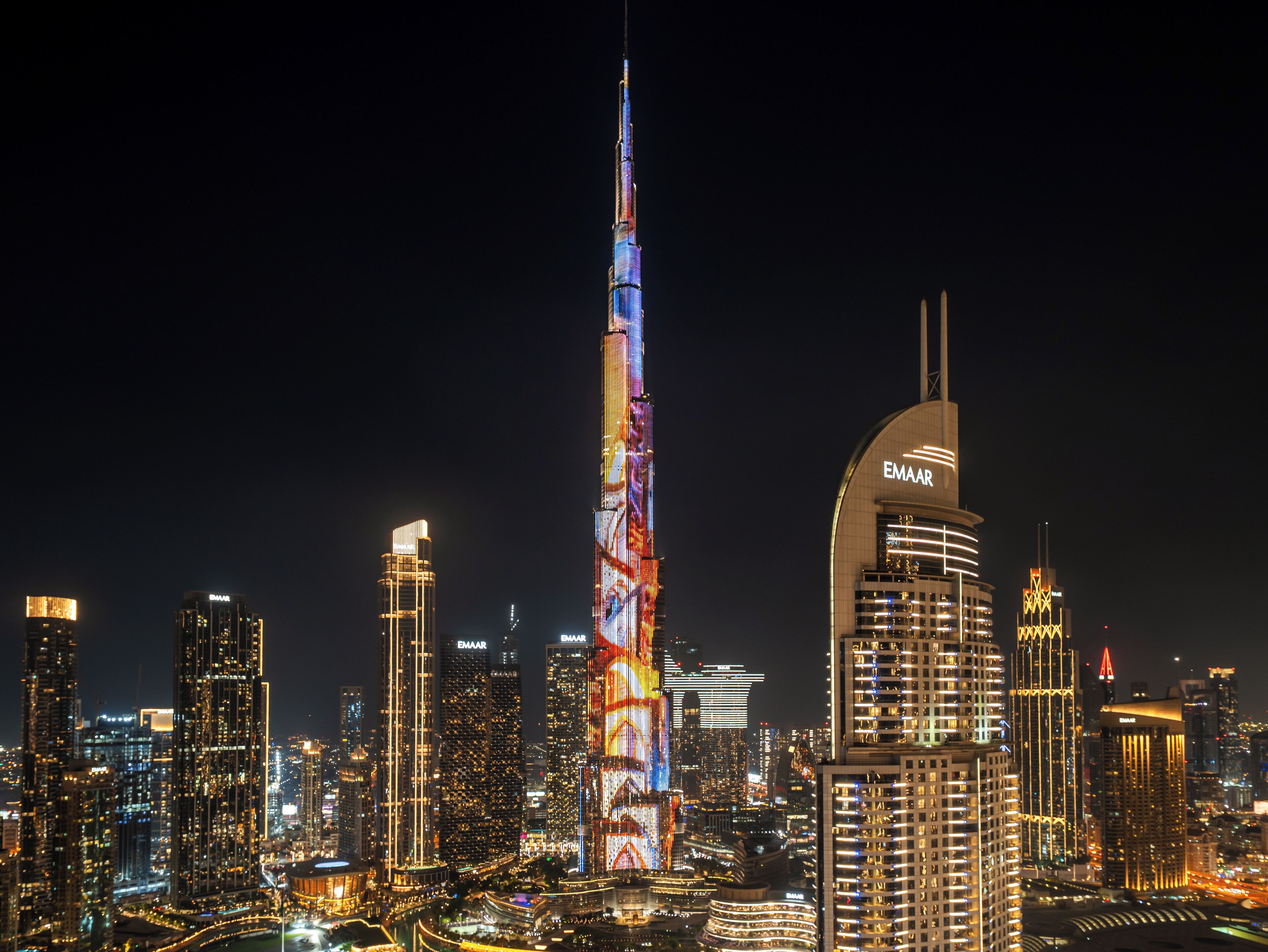 Een stadsgezicht met de Burj Khalifa, verlicht in de nacht, omringd door andere hoge gebouwen.