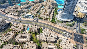 An aerial view of a modern urban area with high-rise buildings, a central roundabout, and a large blue water feature. - ABI Holidays Burj Royale Fountain Views (Dubai)