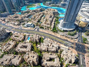 An aerial view of a modern urban area with high-rise buildings, a central roundabout, and a large blue water feature. - ABI Holidays Burj Royale Fountain Views (Dubai)