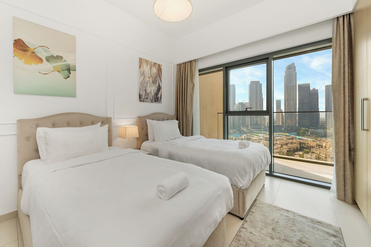 A modern hotel room with two beds, a large window with a city view, and artwork on the walls.