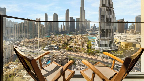 A balcony with two wooden chairs, overlooking a cityscape with high-rise buildings, including the Burj Khalifa. - ABI Holidays Burj Royale Fountain Views (Dubai)