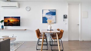 A modern living room with a dining area, featuring a flat-screen TV, artwork, and a thermostat. - Renovated 2-Bed Apartment with Balcony (St Kilda)