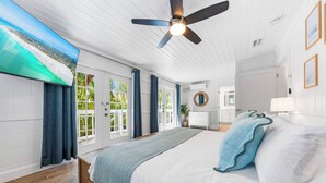 Um quarto espaçoso com uma cama grande, um ventilador de teto e vista para a praia através de uma janela ampla.