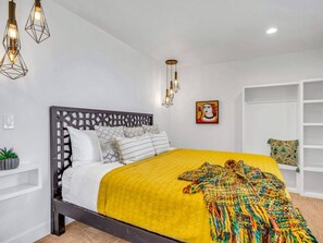 Une chambre à coucher moderne avec un lit, des coussins décoratifs, une courtepointe jaune et une étagère fixée au mur.