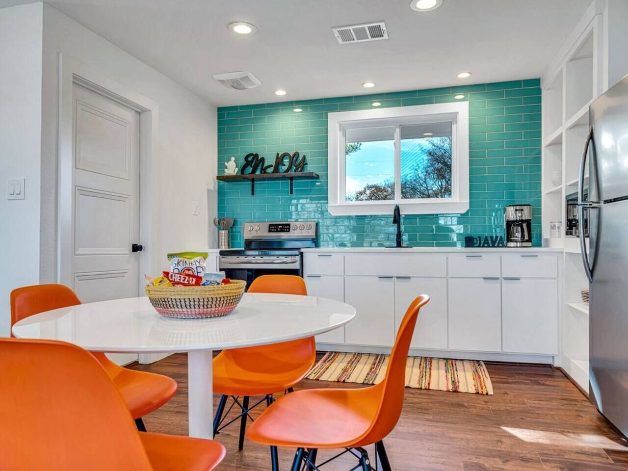 Een moderne keuken met een blauwgroene achterwand, witte kastjes en een raam met uitzicht op de omgeving.