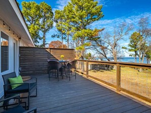 Une terrasse en bois avec des meubles d’extérieur, une vue sur les arbres et un plan d’eau.