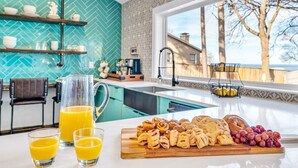 A modern kitchen with a herringbone tile backsplash, a large window with a view of trees, and a breakfast spread on the counter. - Lago Vista- Waterfront | Kayaks | Views! (Wills Point)