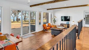 A spacious living area with a wooden deck, a dining table with orange chairs, and a sofa. - Lago Vista- Waterfront | Kayaks | Views! (Wills Point)