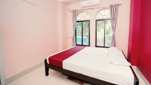 A bedroom with a bed, a window with curtains, and a red wall. - Hotel Nisa (Bolpur)