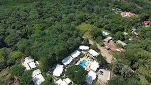 Eine Vogelperspektive zeigt ein Resort mit mehreren Gebäuden mit weißen Dächern, einem Schwimmbad und üppiger, dichter Vegetation ringsum.