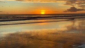 Ein Sonnenuntergang über einem Strand mit Wellen und wolkenlosem Himmel.