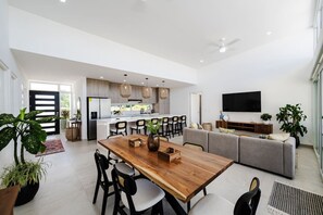 A spacious living area with a wooden dining table, grey sofa, and a TV mounted on the wall. - The Enclave Avellanas - Villa D7 (Playa Avellana)