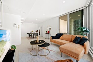 A modern living room with a sofa, a round coffee table, and a dining area with chairs and a table. - Moody Luxe Designer 2BR • Dark Oak • Surry Hills (Surry Hills)