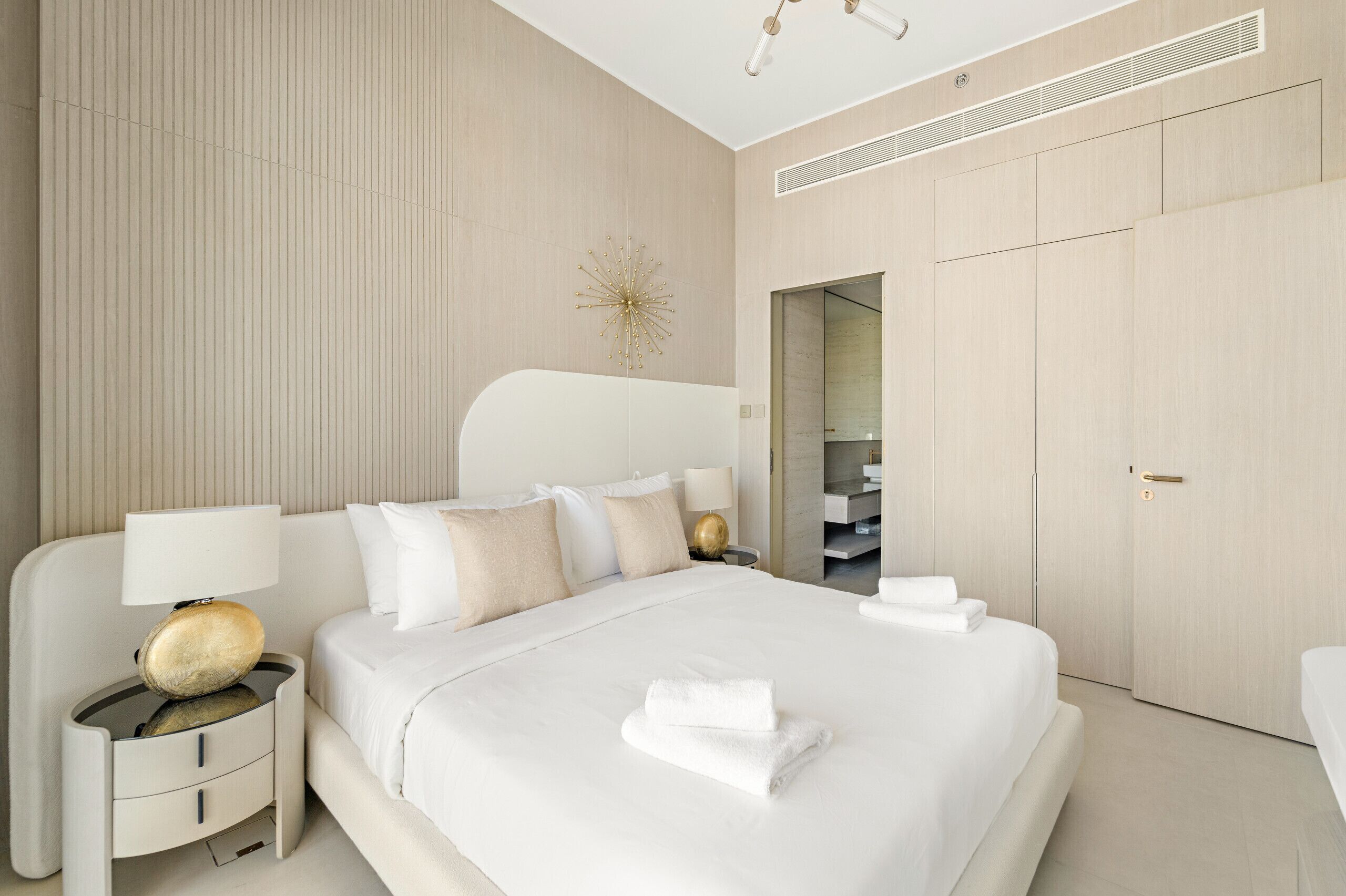A modern hotel room with a large bed, bedside tables, a lamp, and a wardrobe.