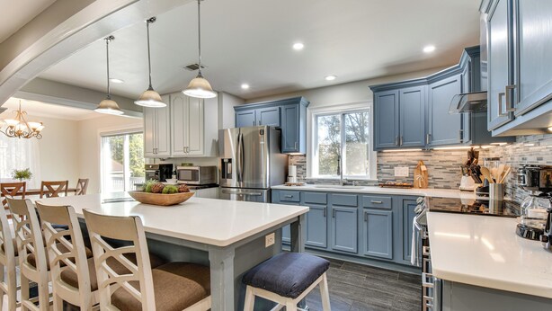 A modern kitchen with white and blue cabinets, stainless steel appliances, and a central island with bar stools. - 4 Seasons of Fun! Walhalla Home w/ Spacious Yard! (Walhalla)