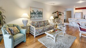 Un salon avec un canapé, des fauteuils, une table basse et un tableau accroché au mur.
