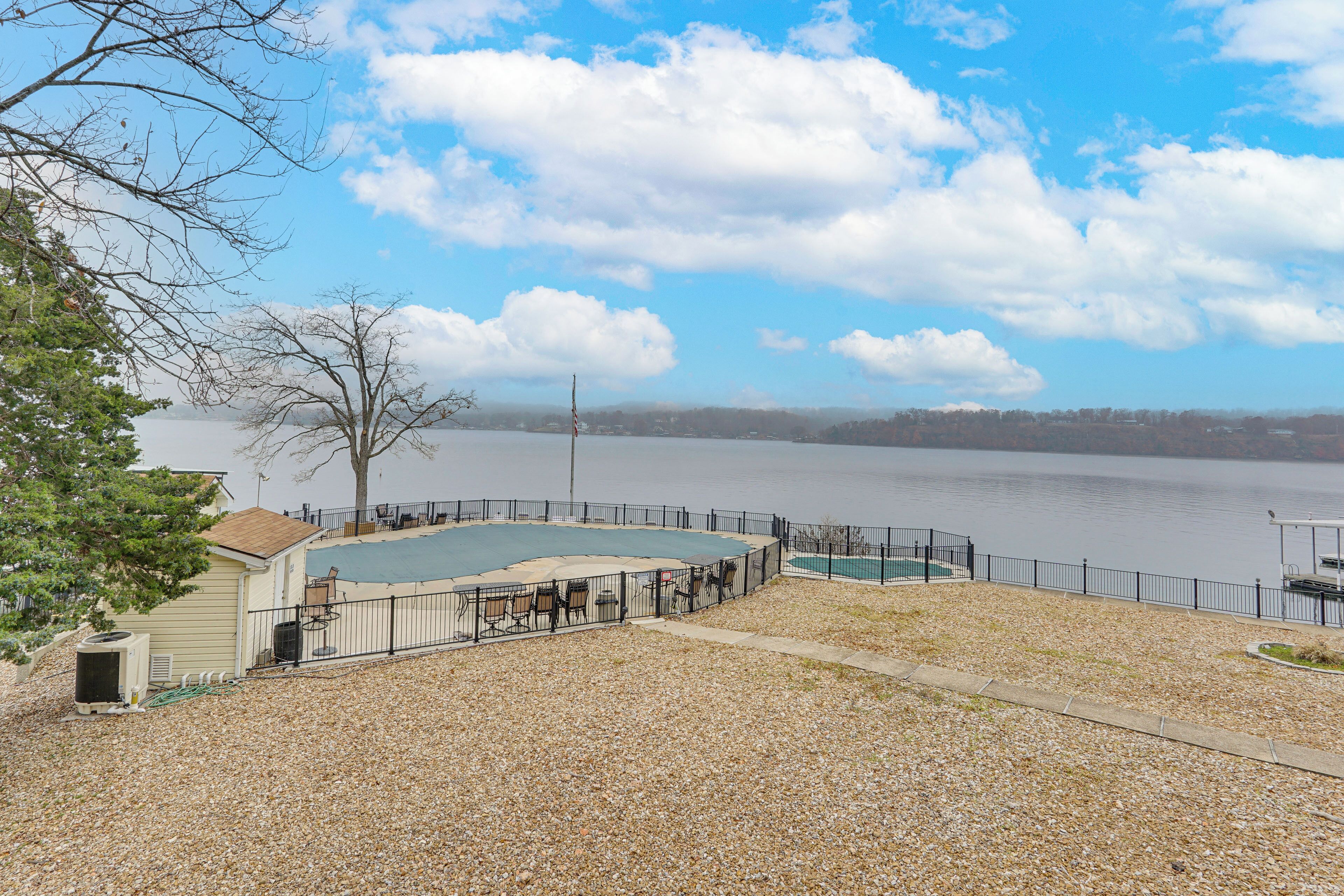 A swimming pool with a fenced deck, a small building, and a view of a lake.