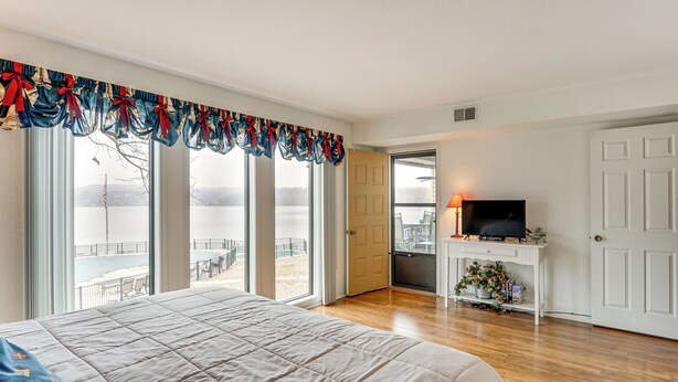 Une chambre avec un grand lit, un téléviseur posé sur un meuble blanc et un balcon donnant sur un plan d’eau.
