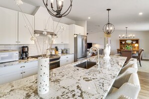 A modern kitchen with white cabinets, a large marble island, stainless steel appliances, and a dining area with a wooden table and chairs. - Scenic Sandia Mtn Views! Cozy Rio Rancho Retreat (Rio Rancho)
