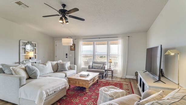 A spacious living room with a large sofa, a coffee table, and a TV. There is a ceiling fan and a window with curtains. - Scenic Sandia Mtn Views! Cozy Rio Rancho Retreat (Rio Rancho)