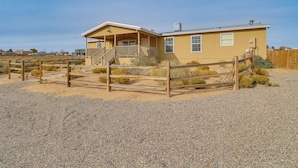 A single-story house with a porch and a covered staircase, surrounded by a wooden fence and gravel ground. - Scenic Sandia Mtn Views! Cozy Rio Rancho Retreat (Rio Rancho)