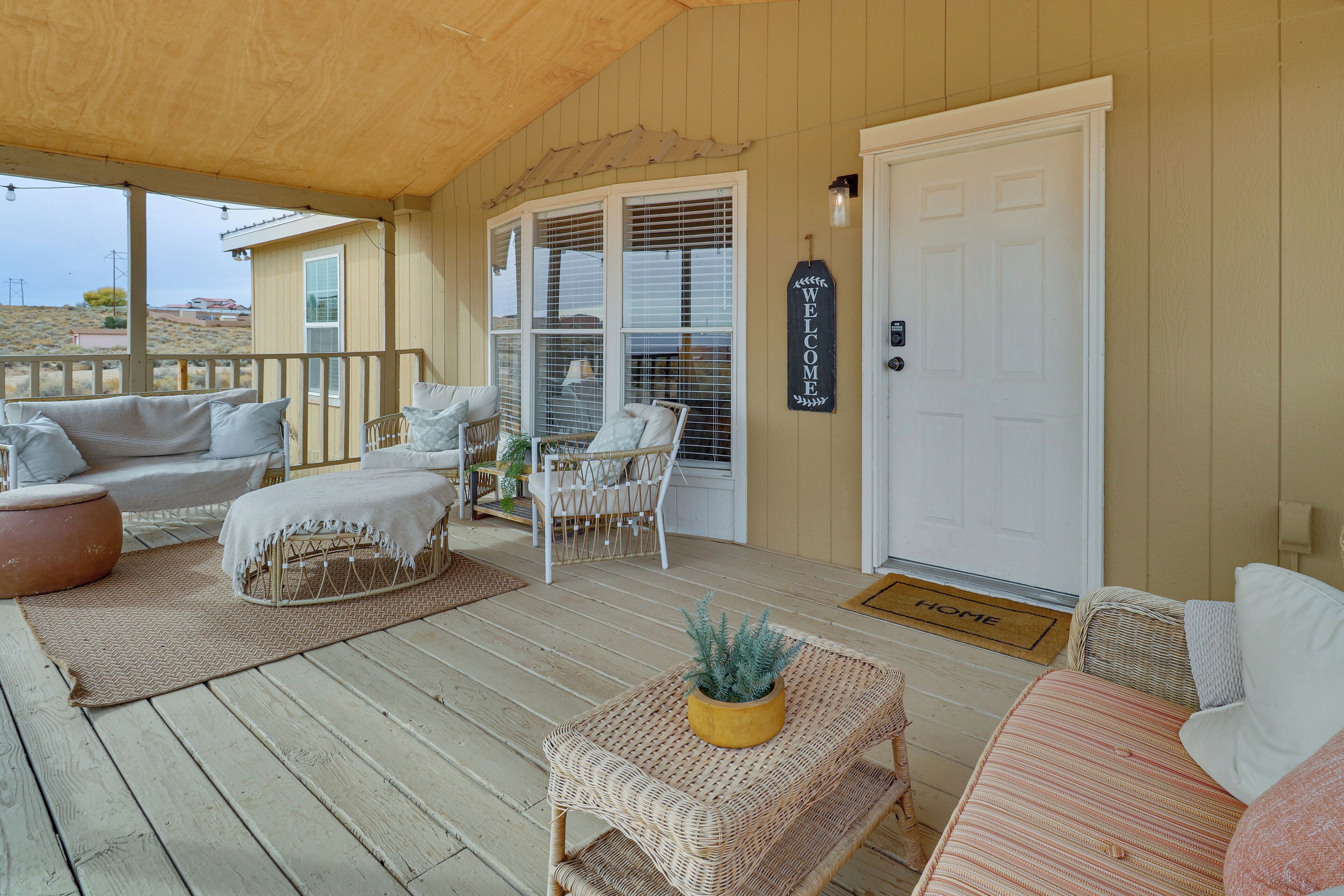 A covered porch with wicker furniture, a welcome sign, and a door with a home doormat.