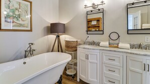 A bathroom with a freestanding bathtub, a vanity with a mirror, and a wicker basket on a small shelf. - Scenic Sandia Mtn Views! Cozy Rio Rancho Retreat (Rio Rancho)