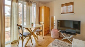 A room with a wooden dining table, chairs, a television on a stand, a wardrobe, and a sliding glass door leading to an outdoor area. - Yard, Deck, Grill! Desert Hideaway By Jemez Canyon (San Ysidro)