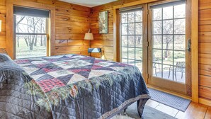 A wooden cabin bedroom with a large bed, a door leading to a patio, and a welcome sign. - 'Mule Creek Lodge' Rural Stay Near Coldwater Lake (Wilmore)