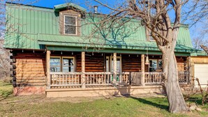 A log cabin with a green metal roof, a porch with railings, and a large tree in front. - 'Mule Creek Lodge' Rural Stay Near Coldwater Lake (Wilmore)