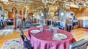 A rustic dining area with a round table set for a meal, wooden beams on the ceiling, and a kitchen in the background. - 'Mule Creek Lodge' Rural Stay Near Coldwater Lake (Wilmore)