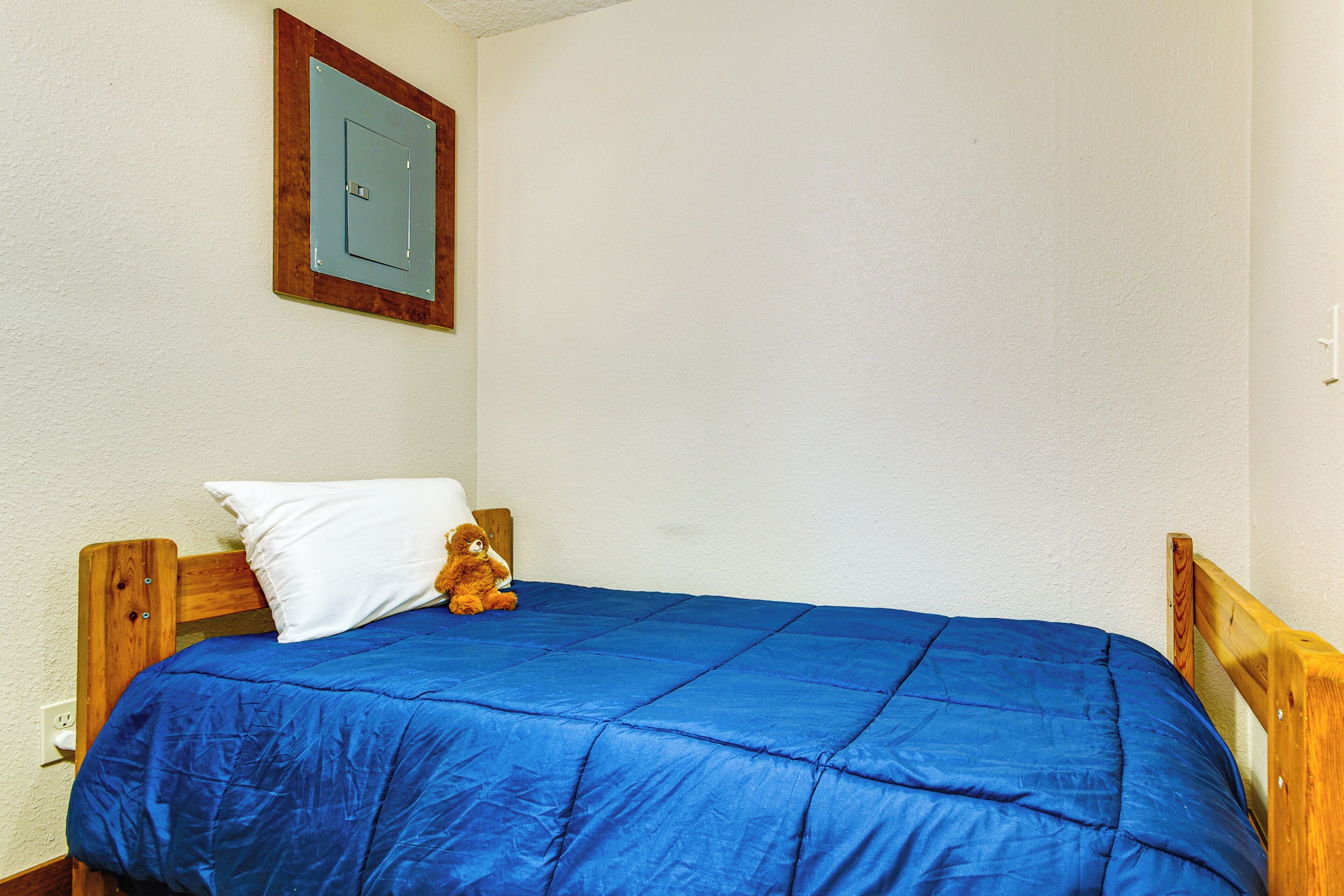 A single bed with a blue mattress and a wooden headboard, a white pillow, and a teddy bear on the bed.