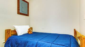 A single bed with a blue mattress and a wooden headboard, a white pillow, and a teddy bear on the bed.