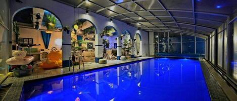An indoor swimming pool with a blue-lit floor, arched ceilings, and various plants and decorations.