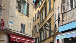 Une rue étroite bordée d’immeubles, un bar appelé « LE SAUVEUR » et un magasin fermé, sur lequel on peut lire l’inscription « Marie Louise ».