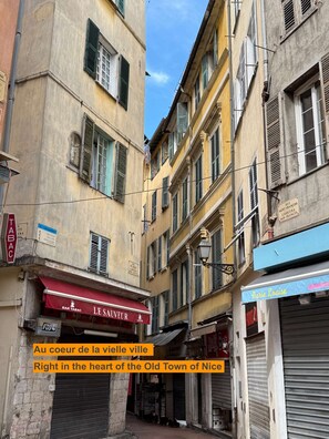 Eine enge Straße mit Häusern, einer Bar namens 'LE SAUVEUR' und einem Geschäft mit dem Schild 'Marie Louise'.